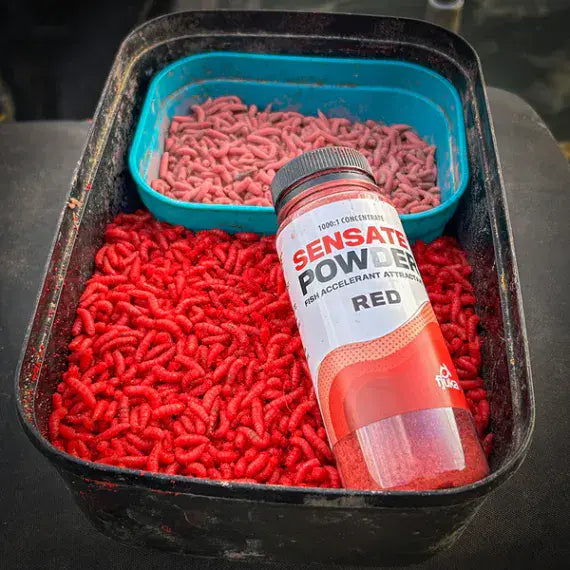 Fjuka Sensate Powder Red bottle placed among red and pink fishing bait maggots in black bait box