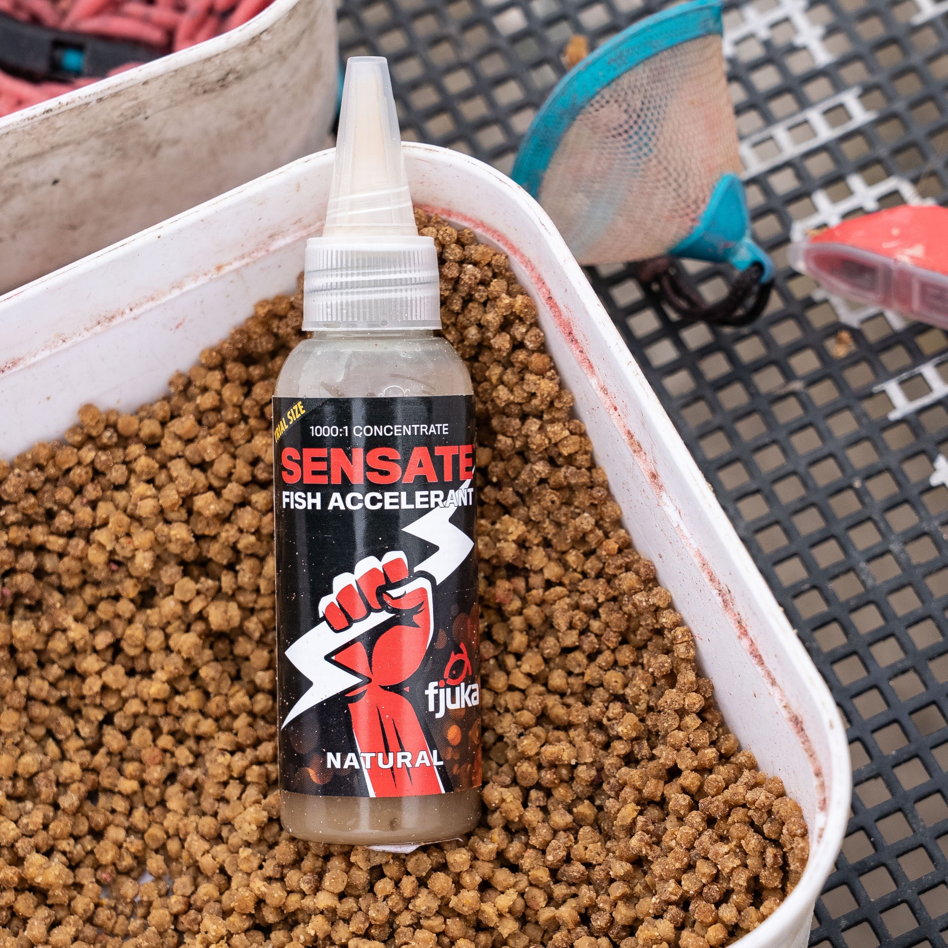 Fjuka Sensate bait enhancer bottle placed on a tray of micro pellets